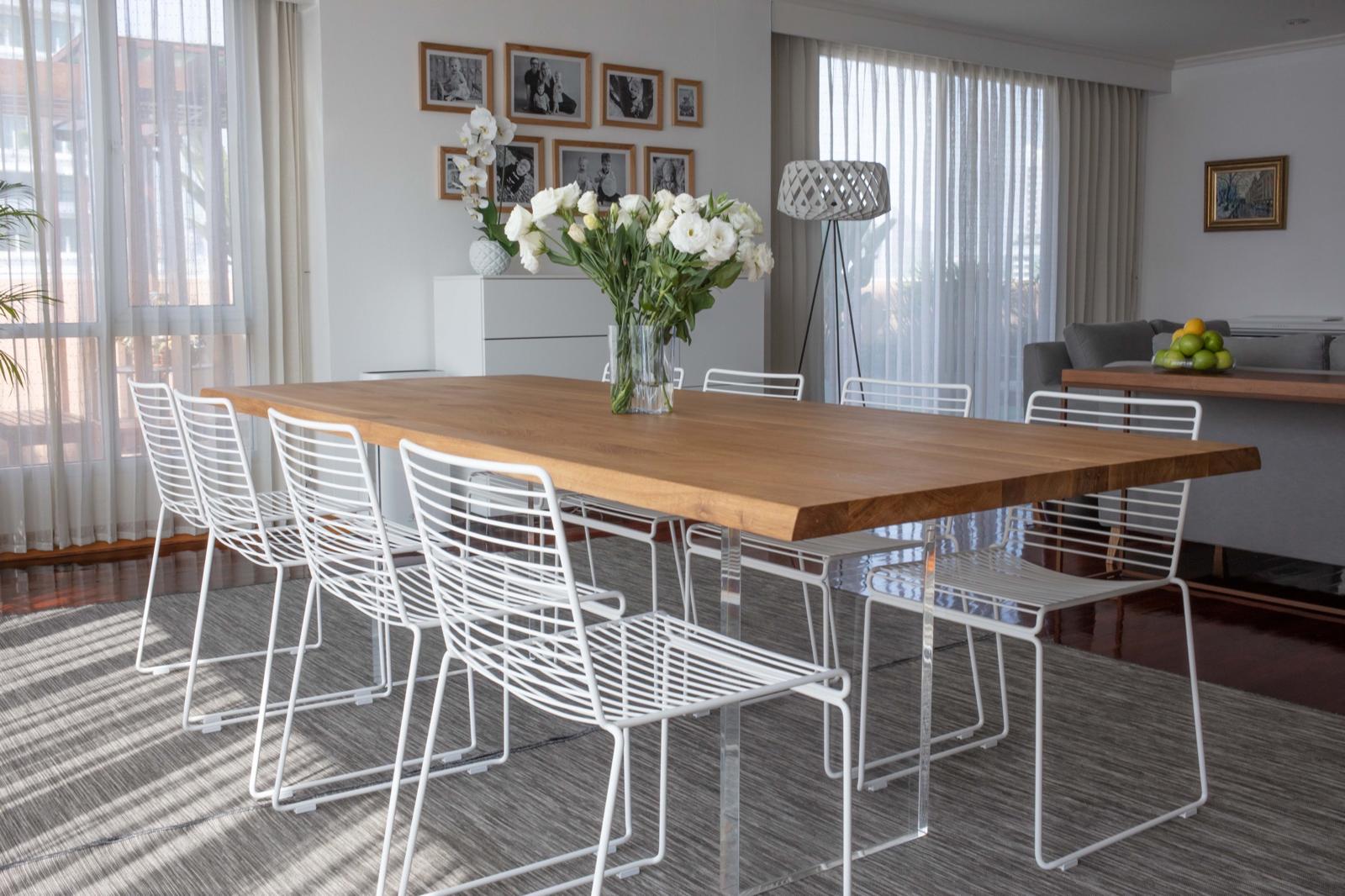 Light-filled dining room with a long wooden table, white wire chairs and fresh white flowers