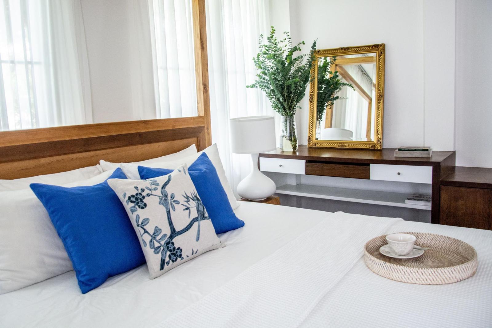 Bright bedroom with natural wood, neutral linens and a blue cushion